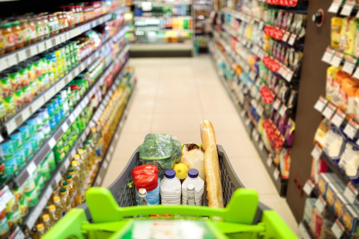 A Shopping Cart Is Filled With Groceries In A Supermarket Aisle