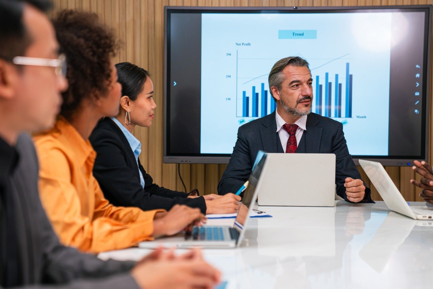 A Man Is Giving A Presentation To A Group Of People In A Conference Room.