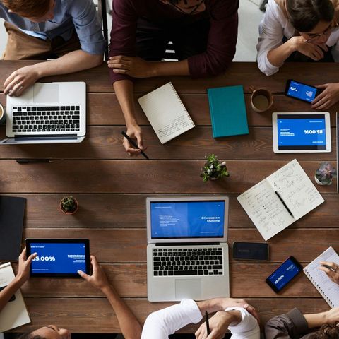 A group of people are sitting at a table with laptops and tablets
