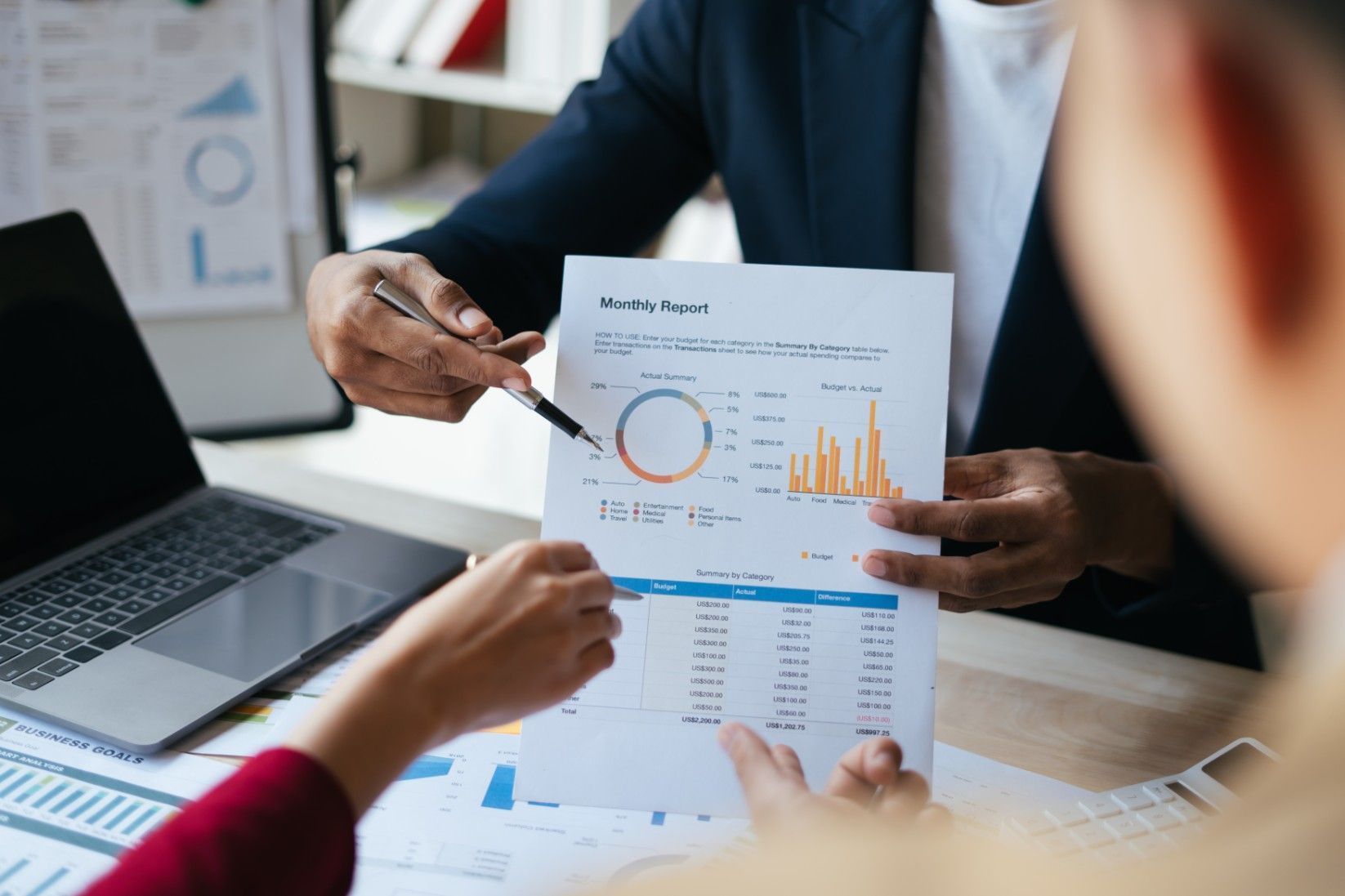 A Man Is Pointing At A Graph On A Piece Of Paper While A Woman Looks On