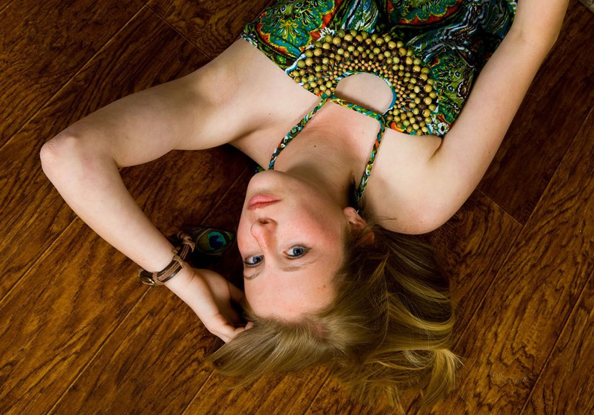 Woman lying on a wooden floor in a green patterned dress, looking at the camera.