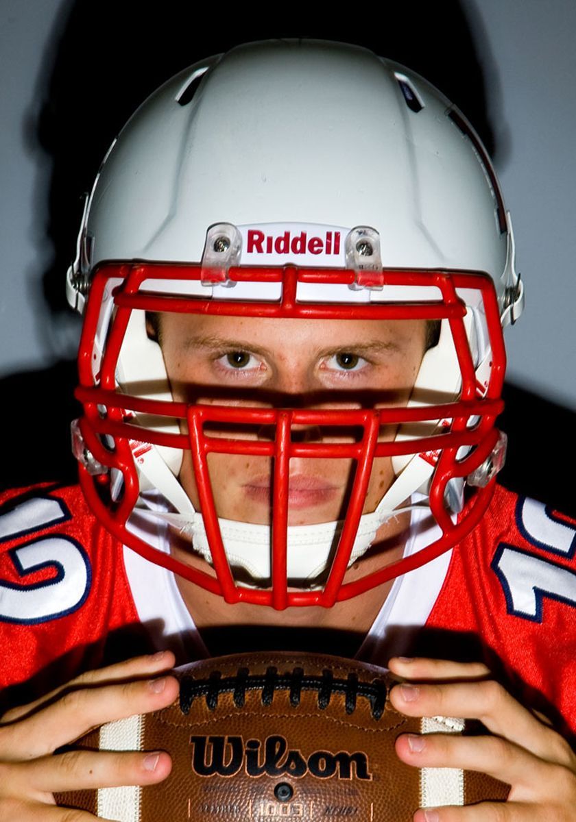 Football player in red helmet and jersey holding a football and staring ahead