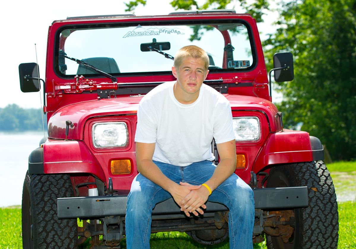 Young man in a white T-shirt and jeans sitting on the bumper of a red Jeep outdoors