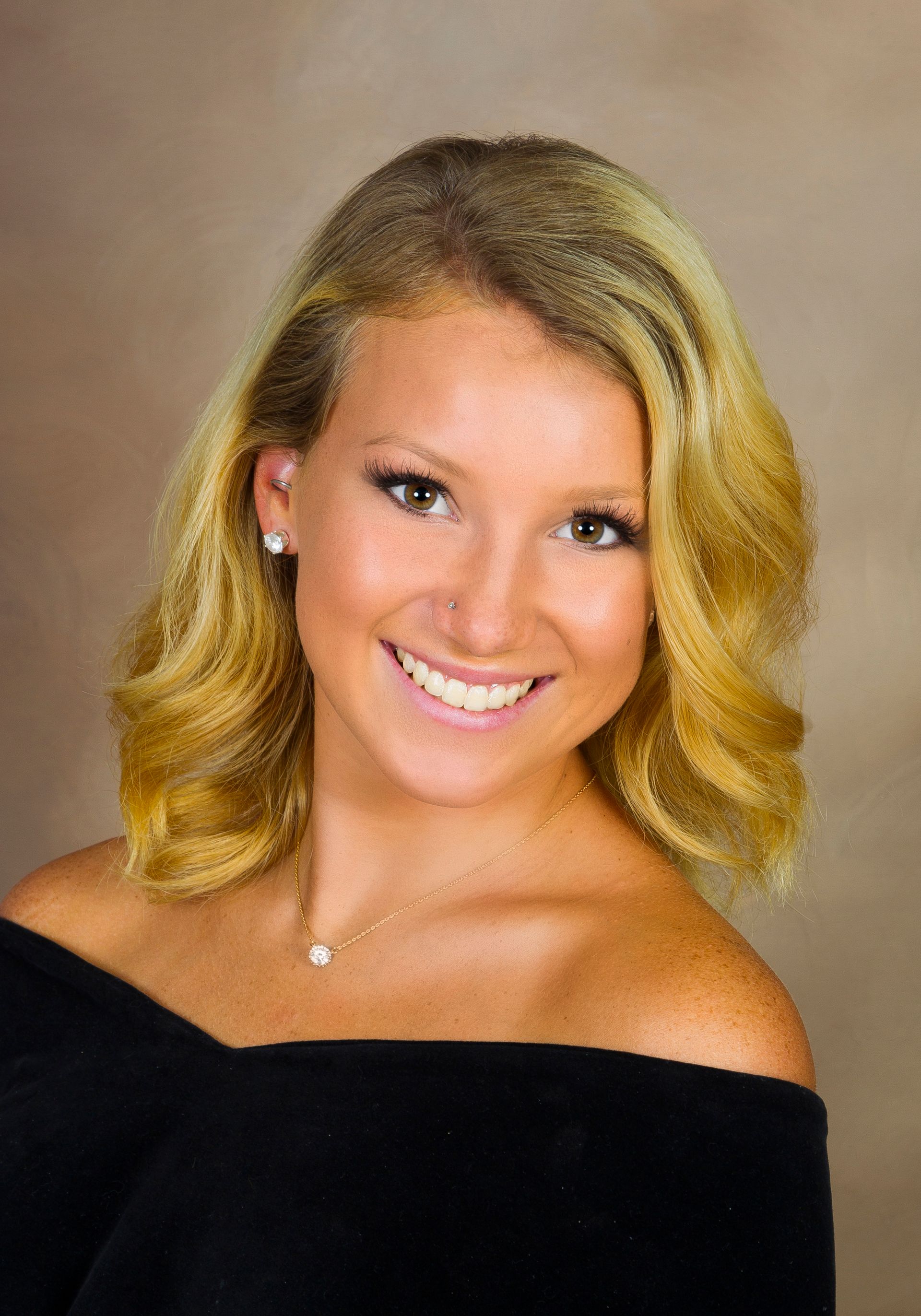 Smiling blonde woman in a black off-the-shoulder top against a neutral backdrop