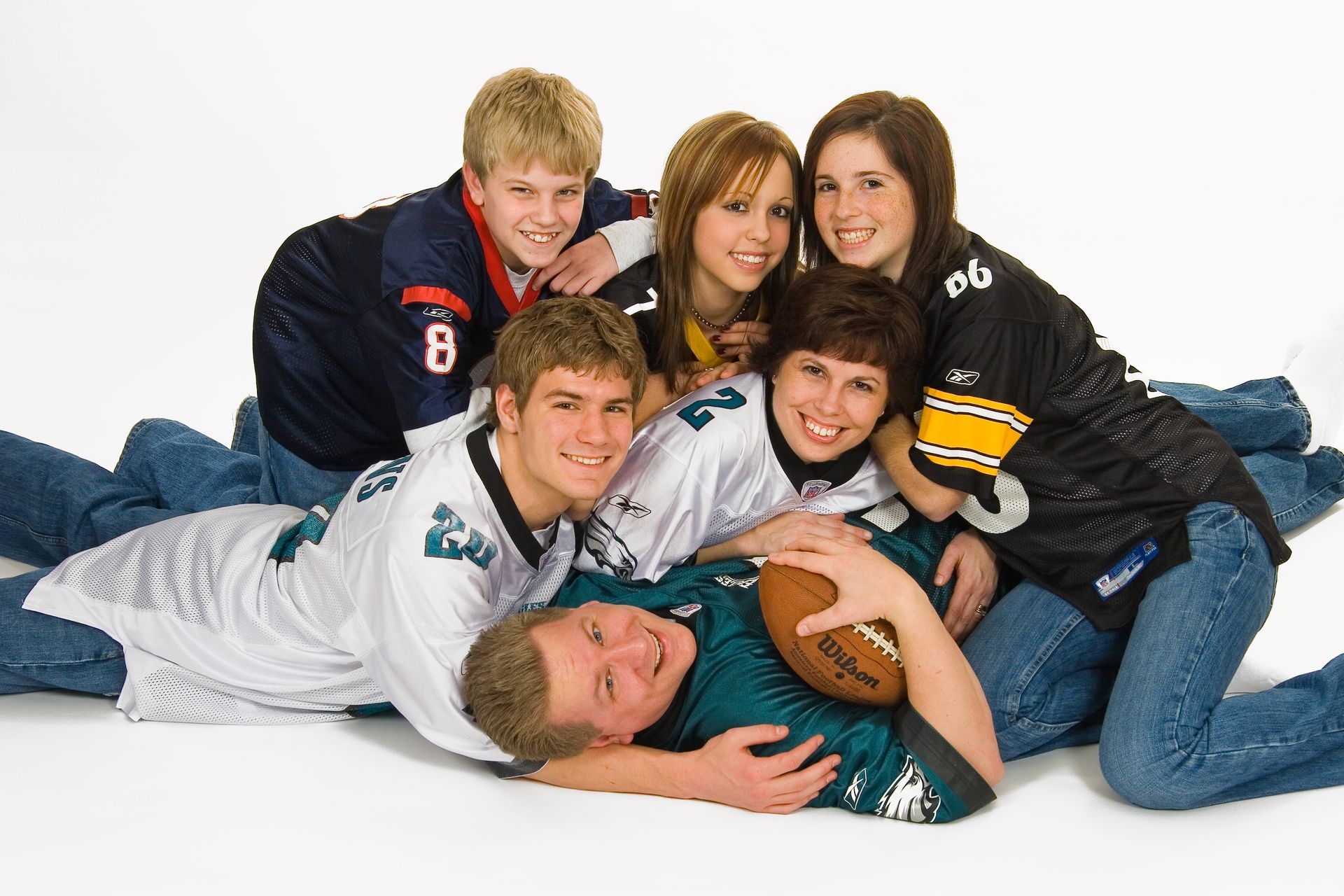 Five smiling people piled together on a white background, posing playfully in sports jerseys