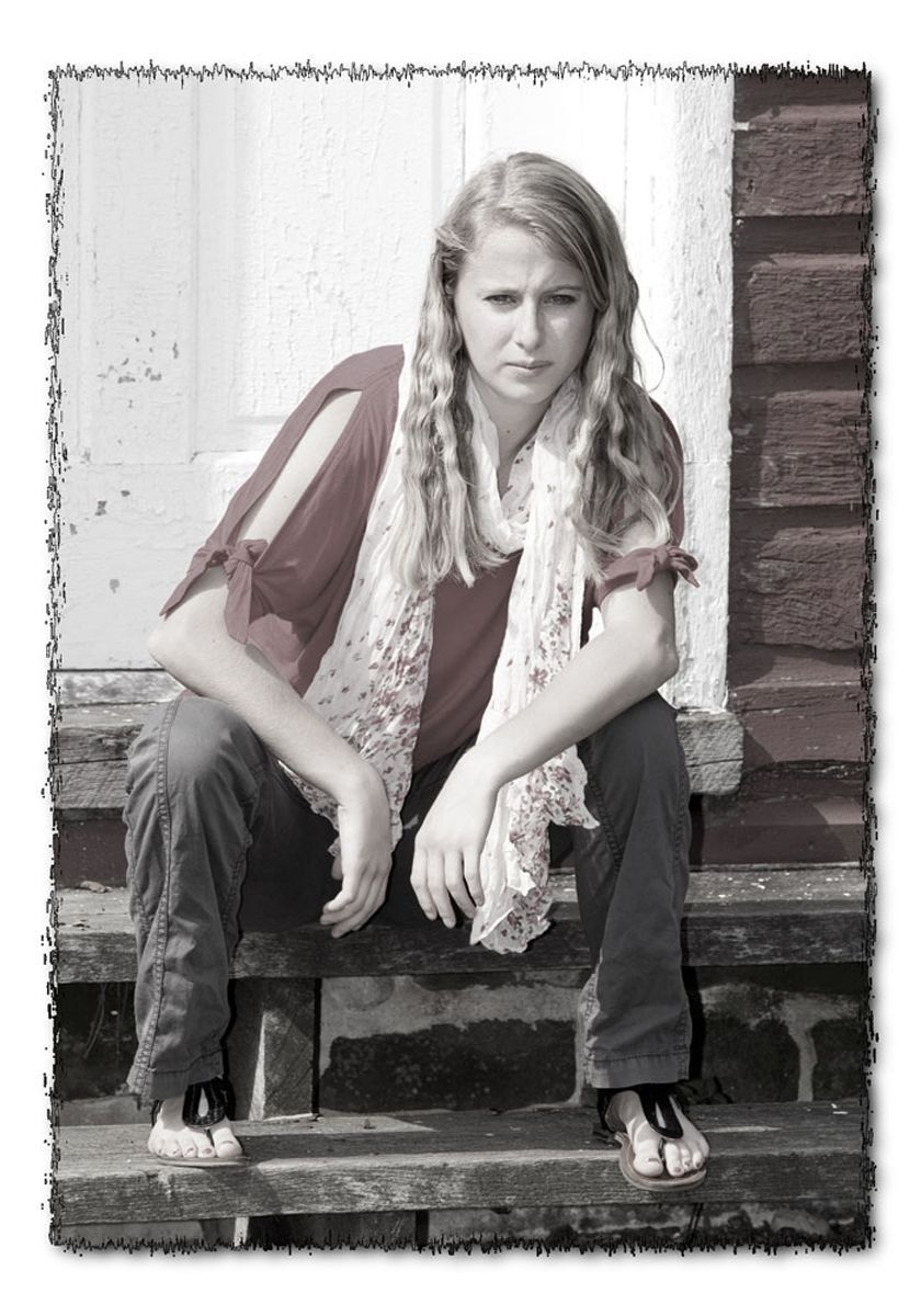 Person sitting on stone steps beside a brick wall, wearing jeans and a scarf, looking at the camera.