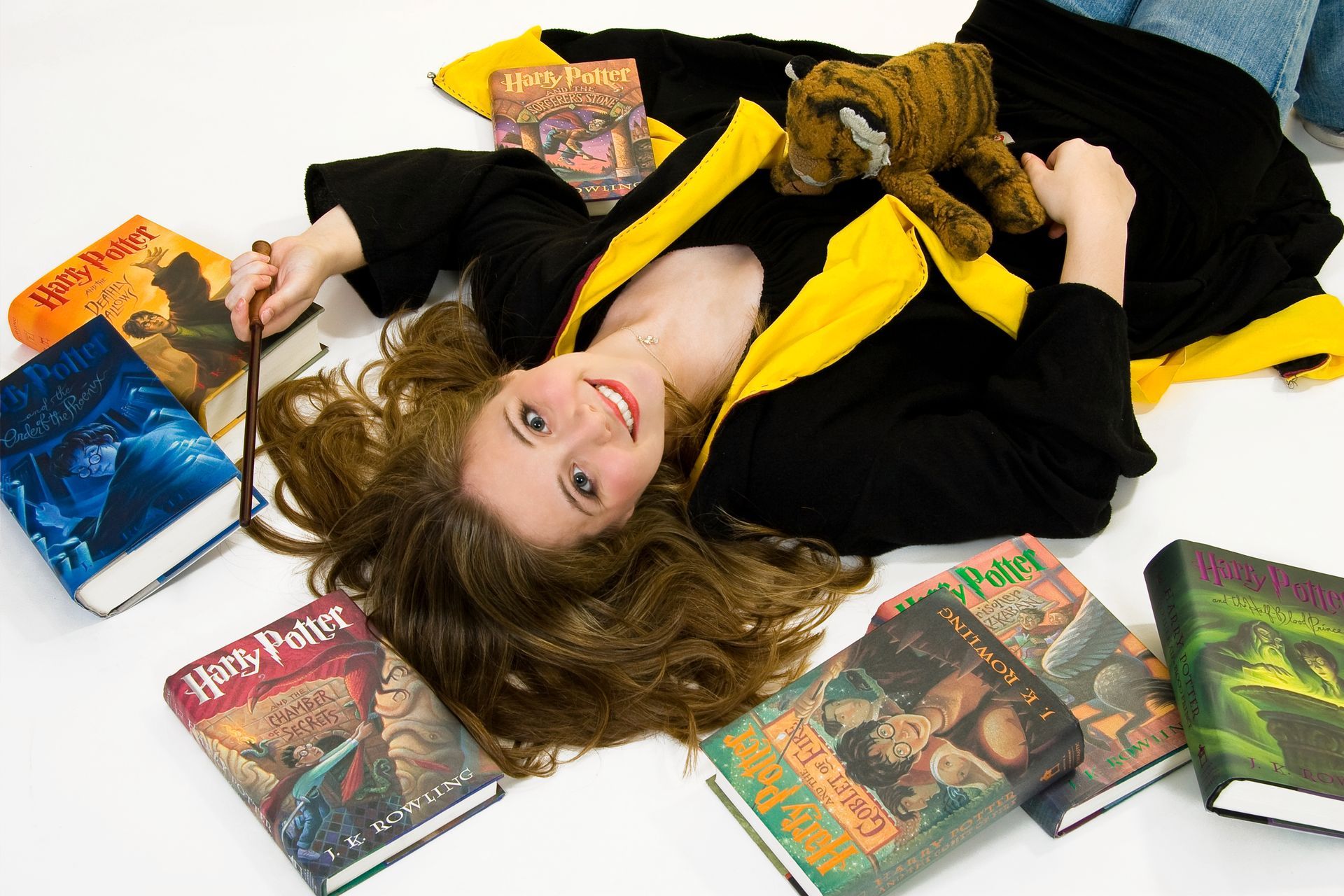 Person lying on a white floor beside several colorful books, wearing a black and yellow outfit.