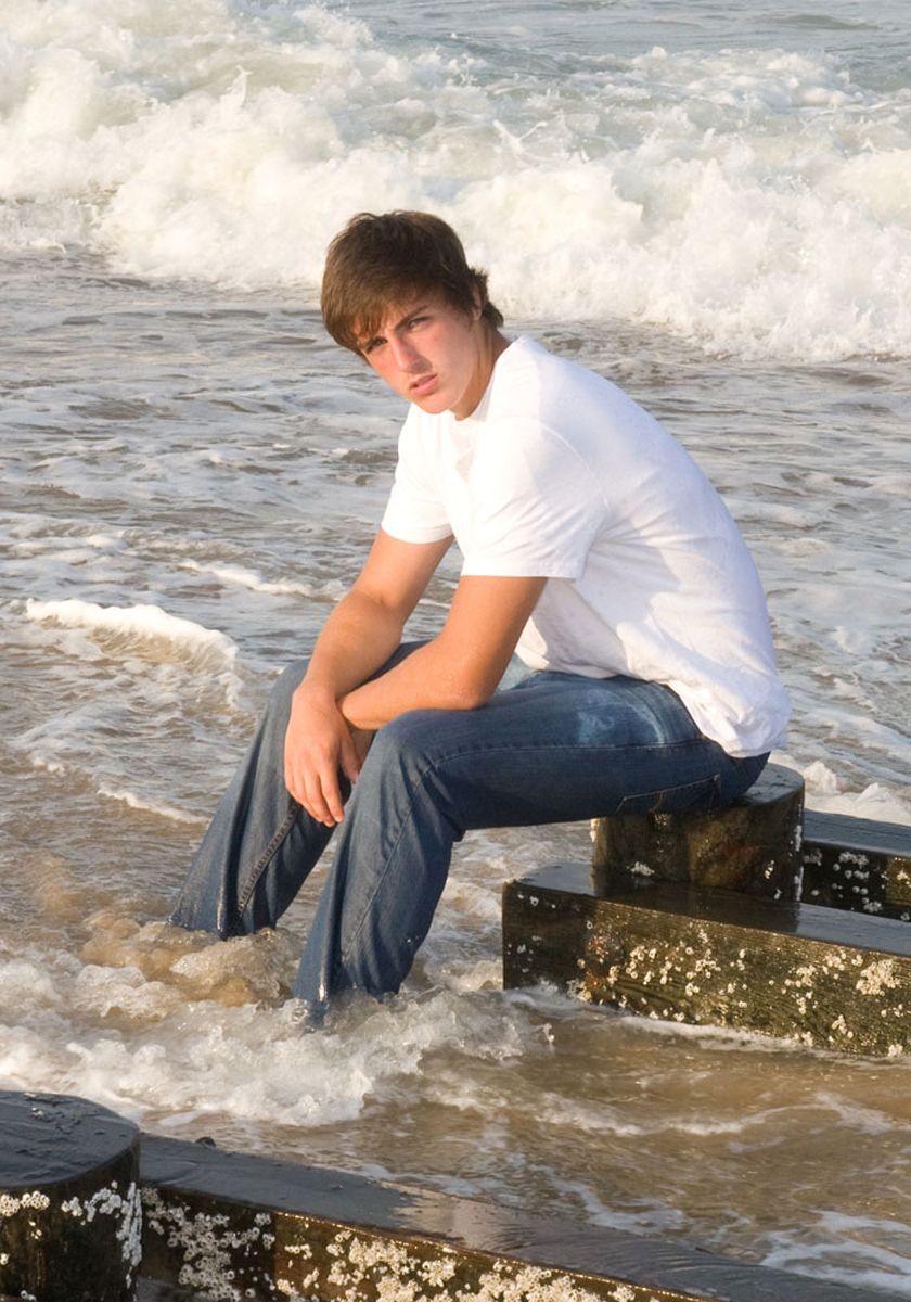 Person sitting on a bench in shallow surf with waves crashing behind them, wearing a white shirt and jeans