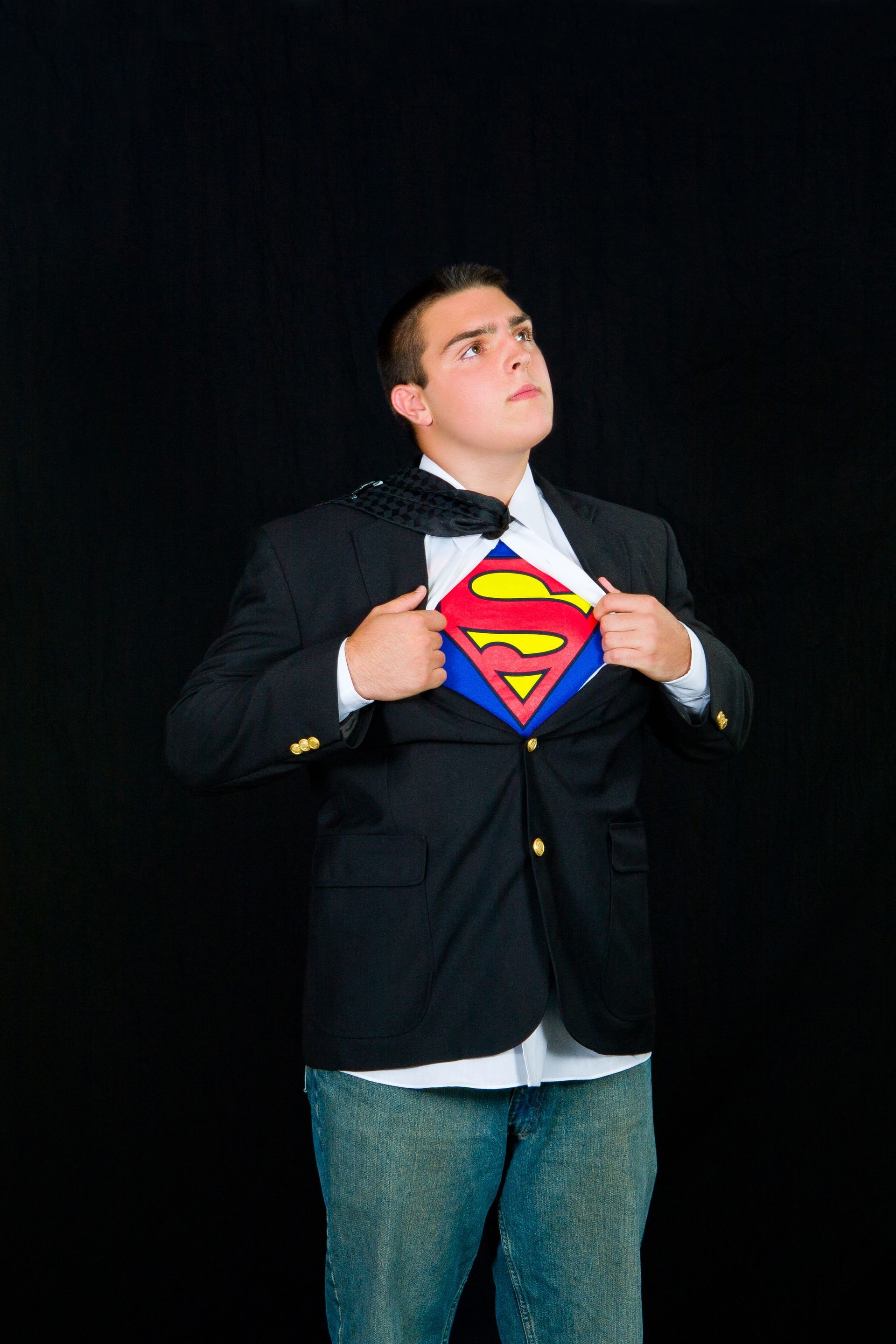 Man in a suit opening shirt to reveal a Superman logo on his chest against a black background
