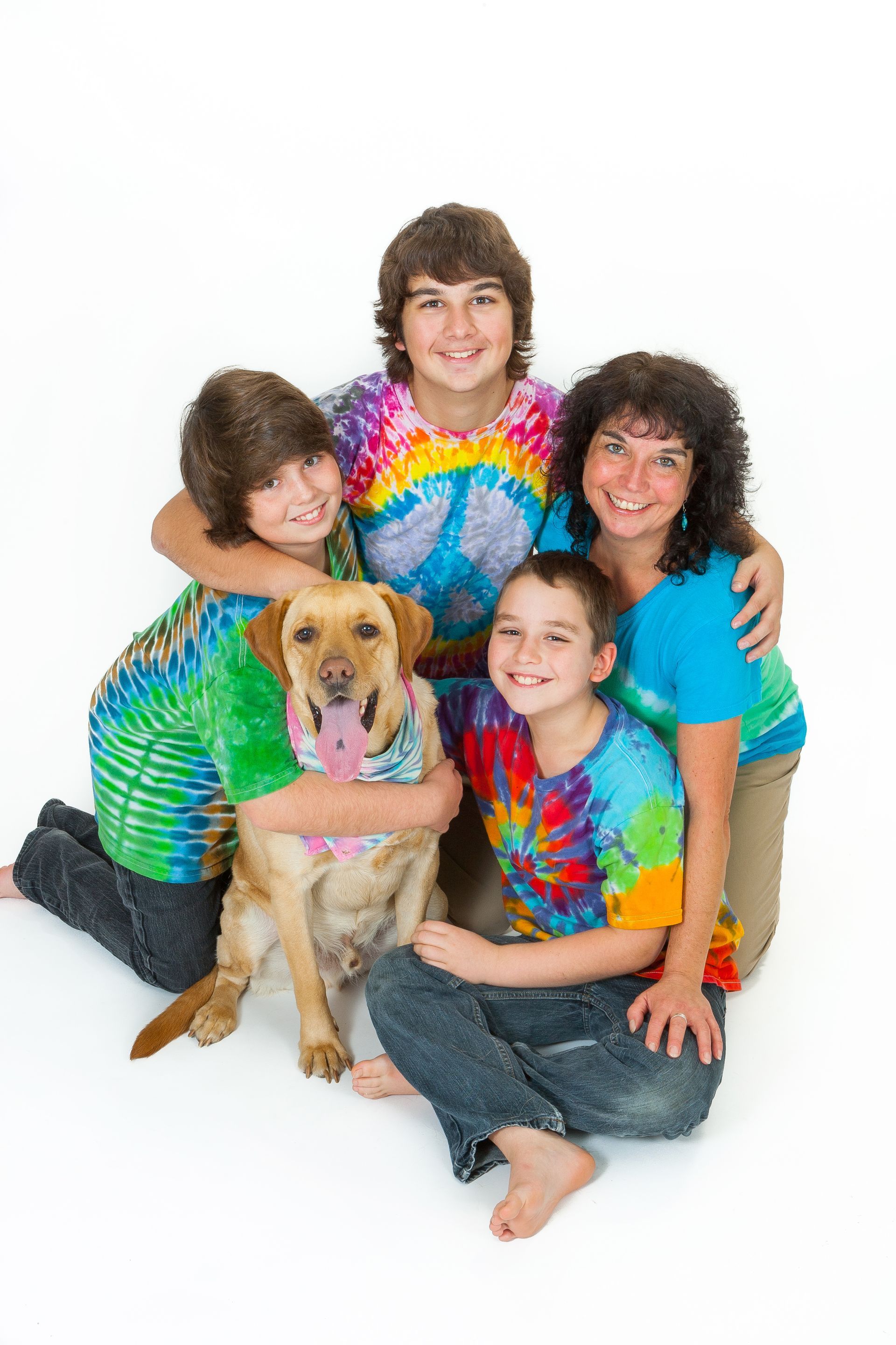 Four people in tie-dye shirts sit with a golden retriever on a white background.