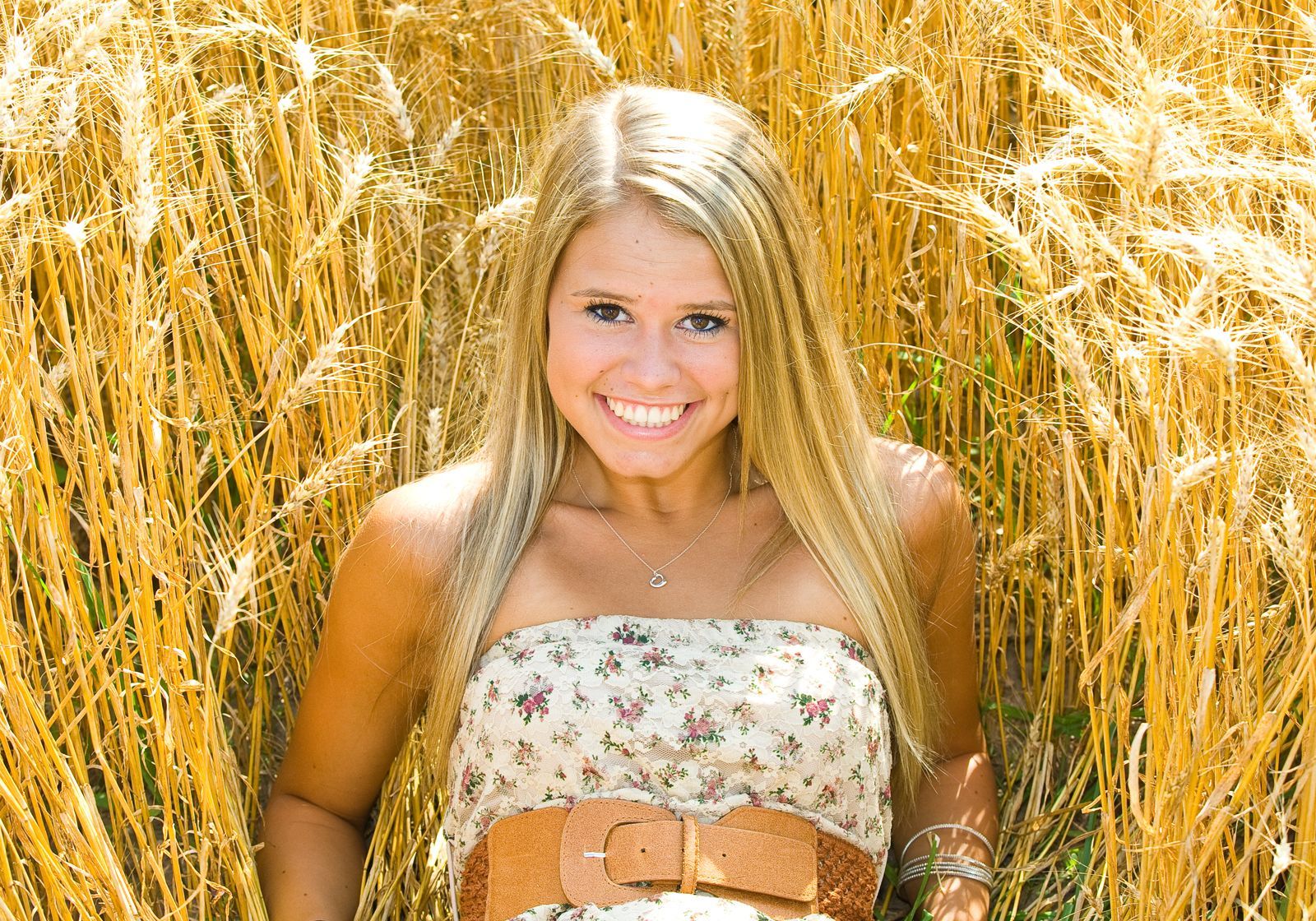 Smiling blonde woman in a floral dress standing in a golden wheat field