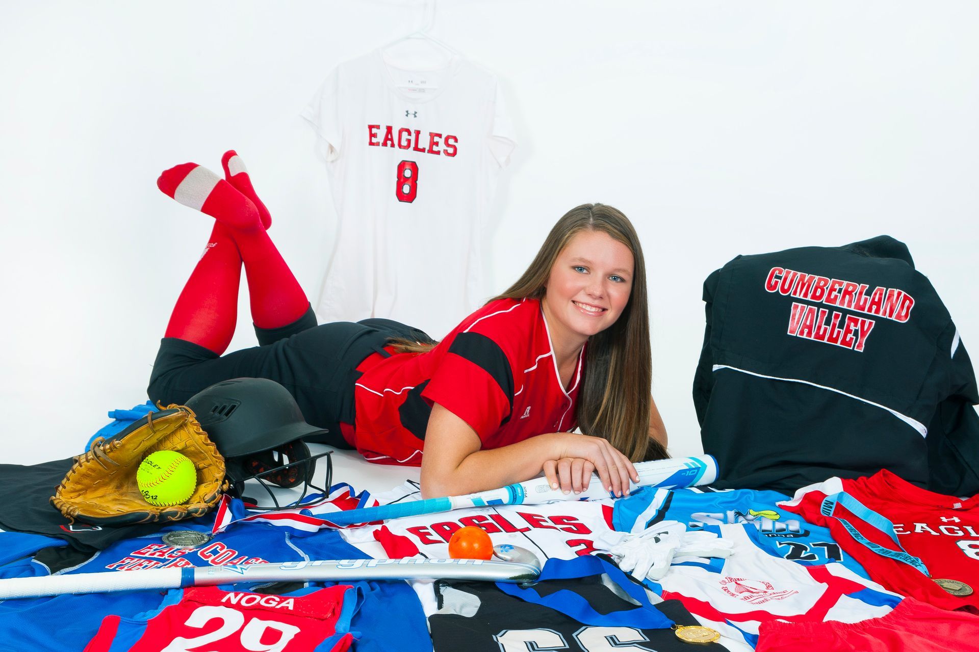 Teen in red Eagles outfit lying on a bed with team shirts and sports gear spread around her