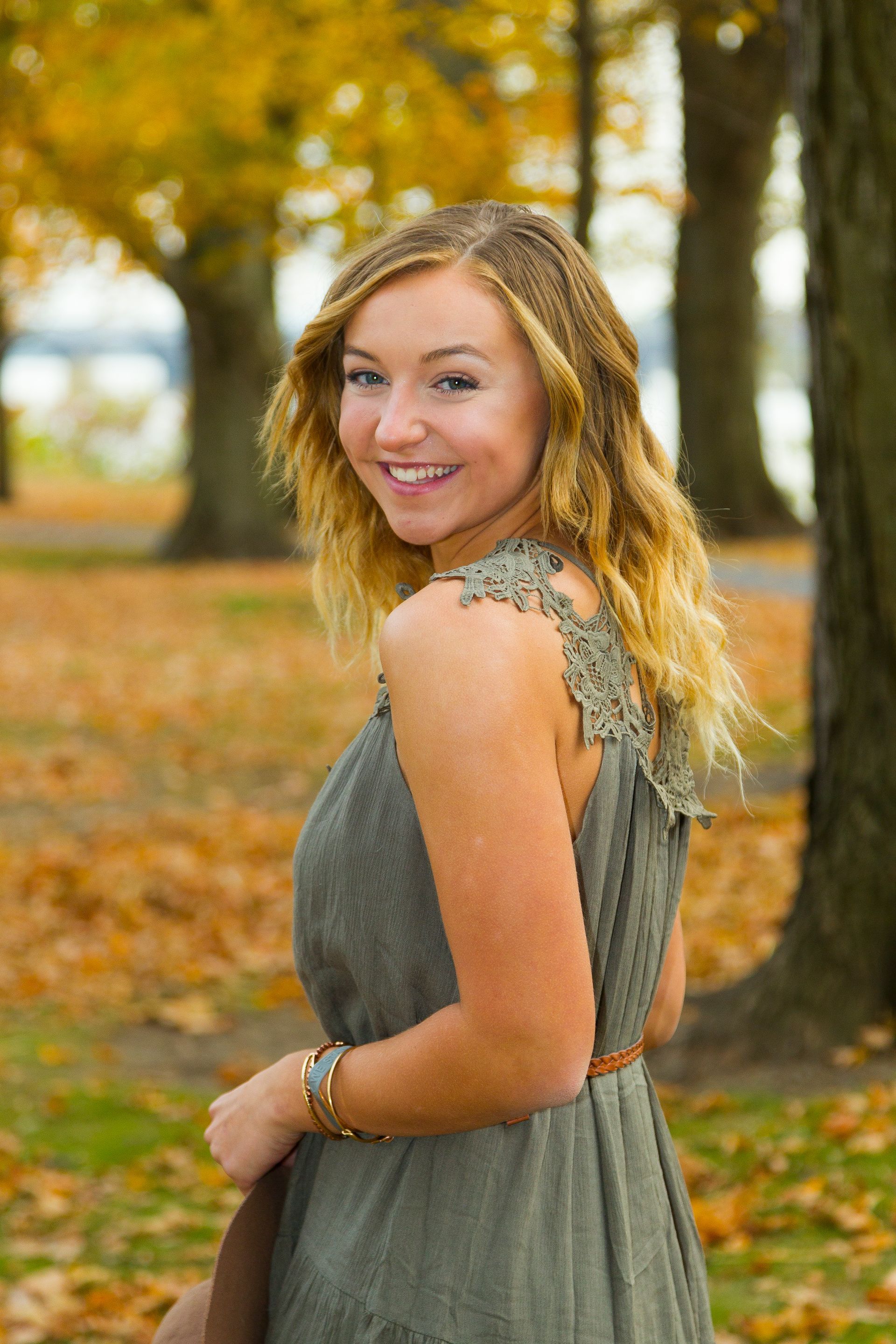 Smiling woman in a green dress standing in an autumn park with trees and fallen leaves