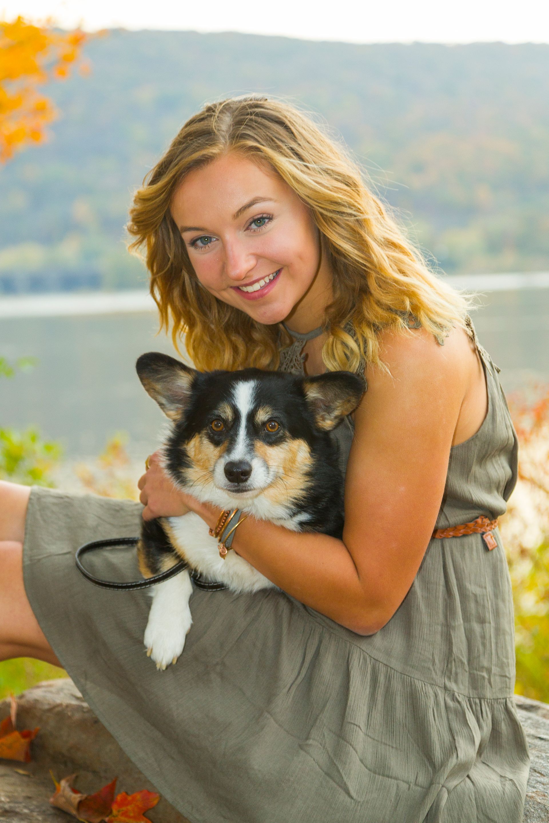 Smiling woman holding a black-and-white dog outdoors by a lake