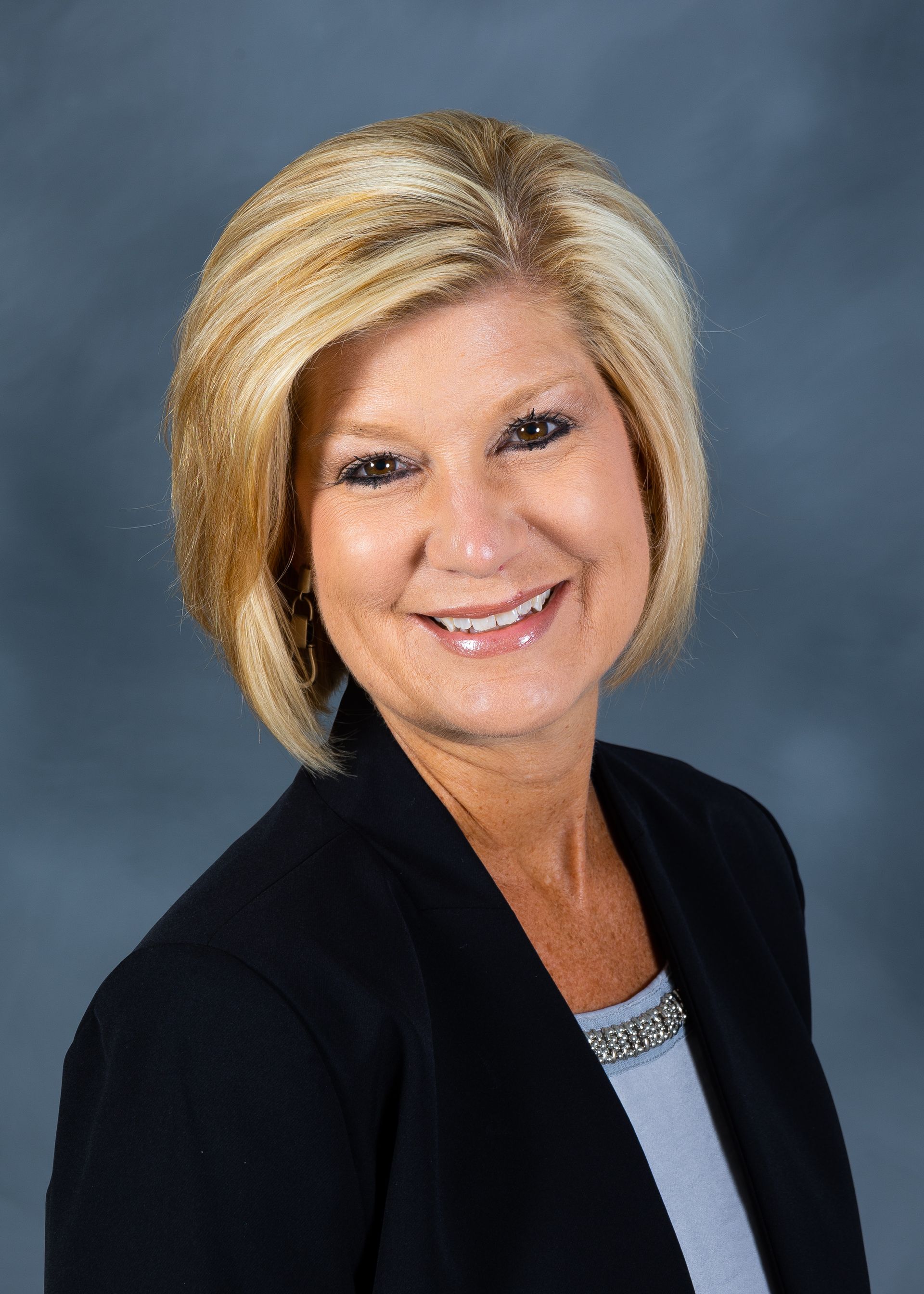 Smiling woman in a black blazer against a blue studio backdrop