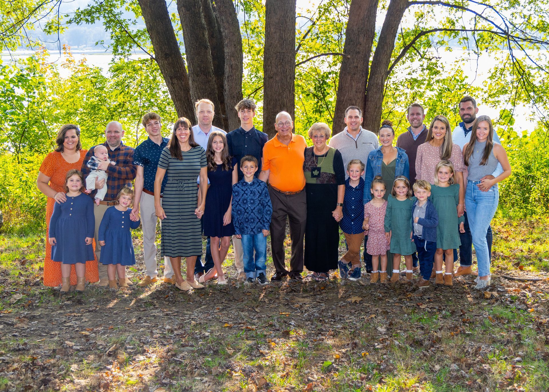Group of people standing outdoors under trees, posing together in fall sunlight.