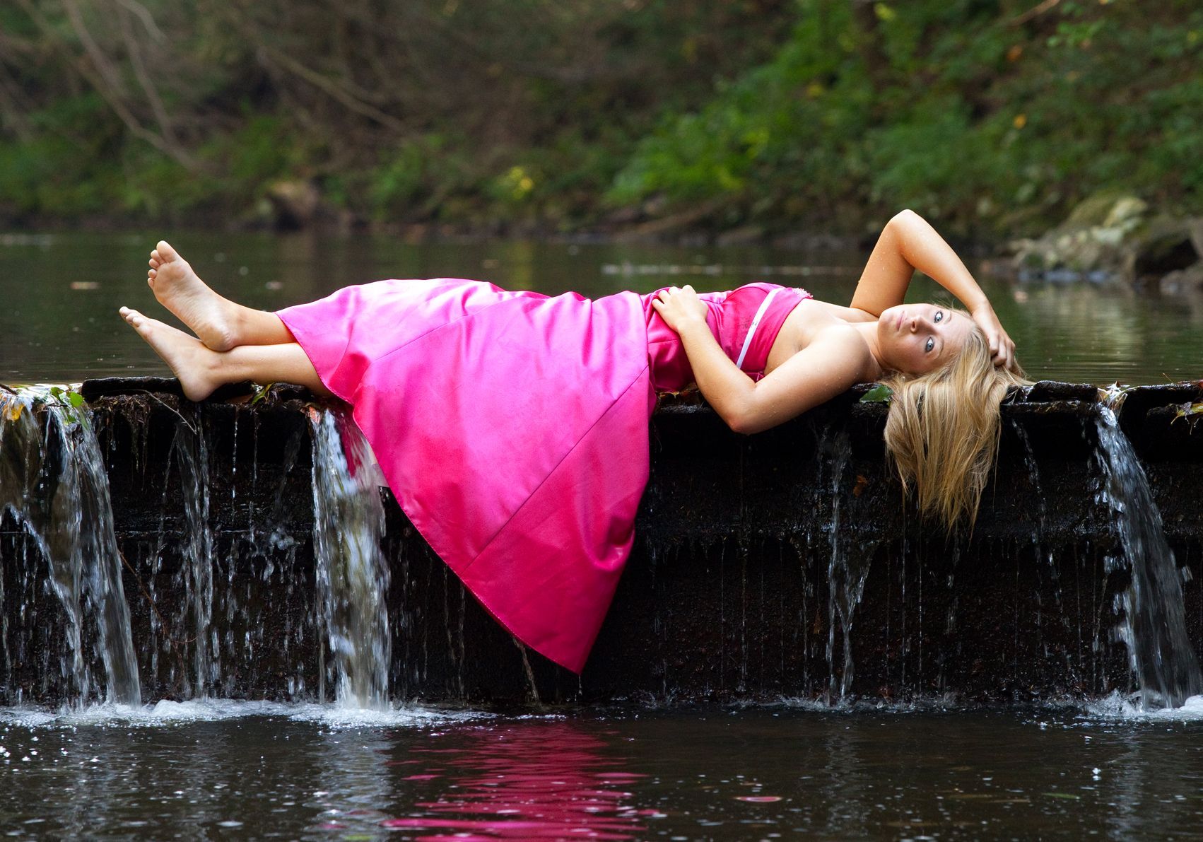 Woman in a bright pink dress reclining on a waterfall ledge above flowing water