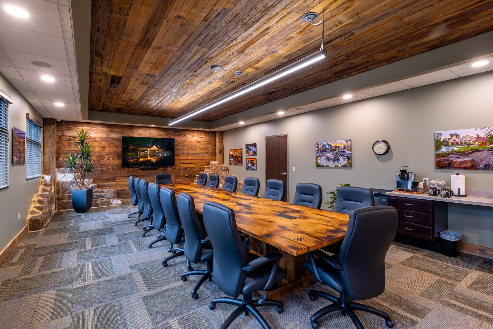 Modern conference room with a long wooden table, blue chairs, wall art, and wood-accent ceiling.