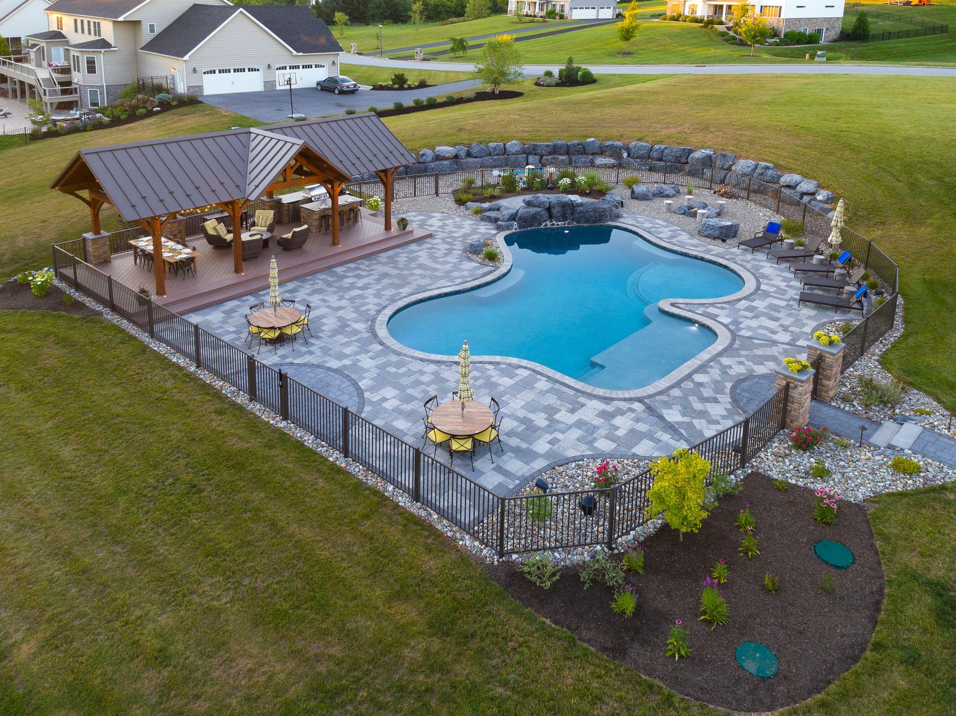 Backyard swimming pool with stone patio, pavilion, and landscaped lawn in a suburban yard
