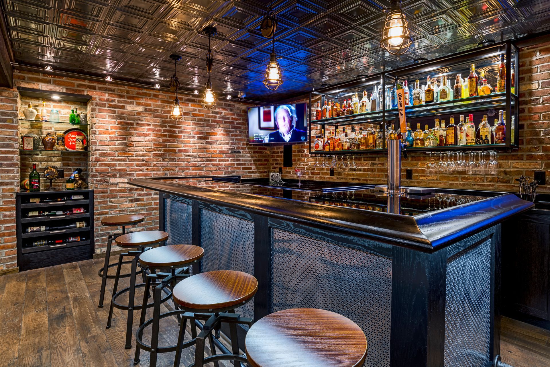 Brick-walled bar interior with a long counter, stools, shelves of bottles, and warm hanging lights