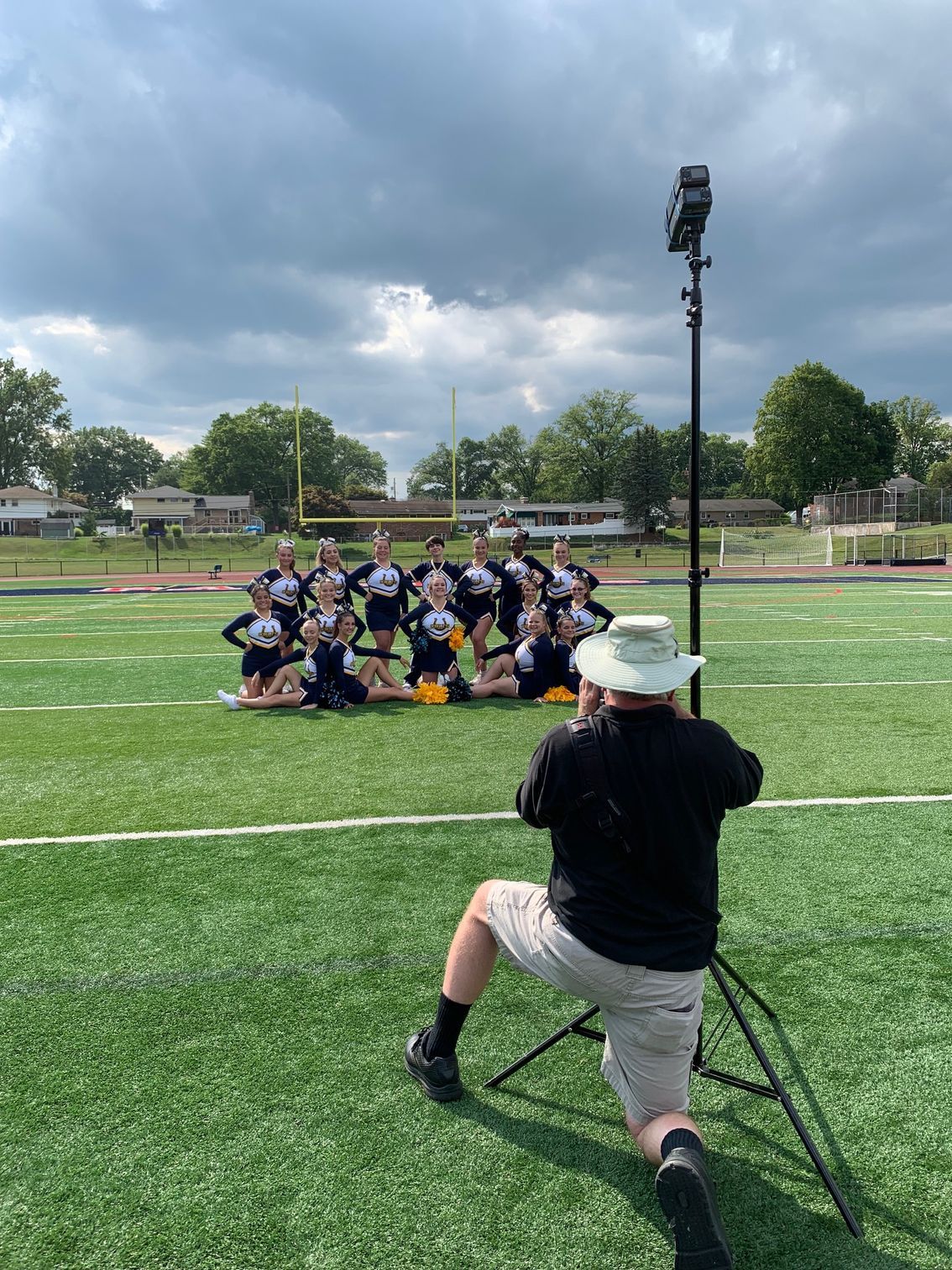 Photographer filming a group pose on a soccer field under cloudy skies