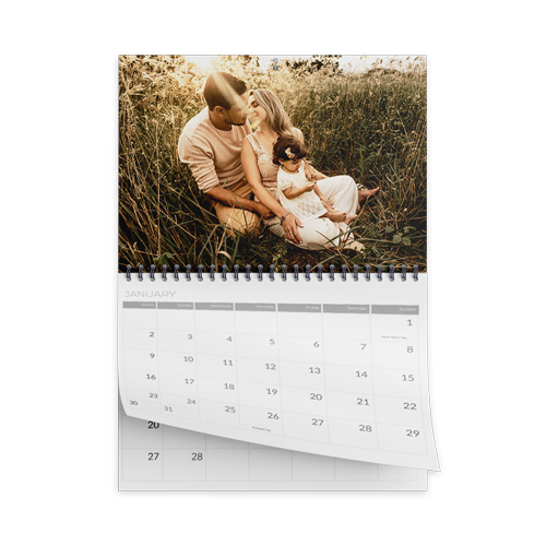 Spiral-bound desk calendar with a photo of a person holding a child sitting in tall grass