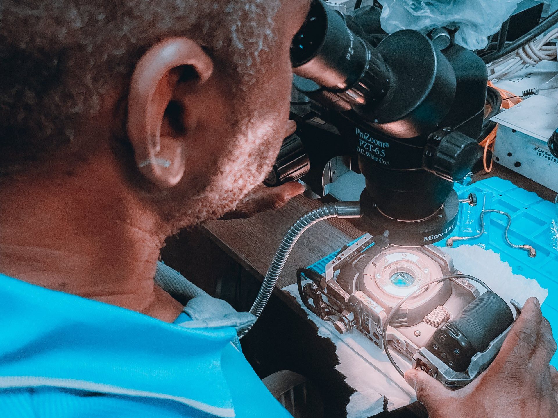 Person using a microscope to inspect a lit smartphone on a workbench