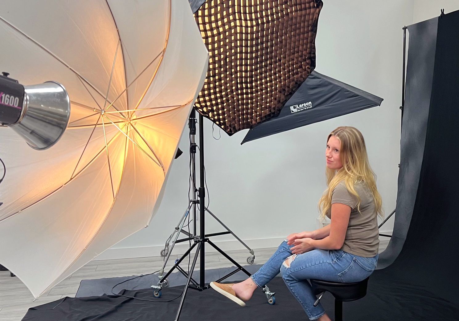 Woman seated in a photo studio beside lighting equipment and a large white umbrella reflector