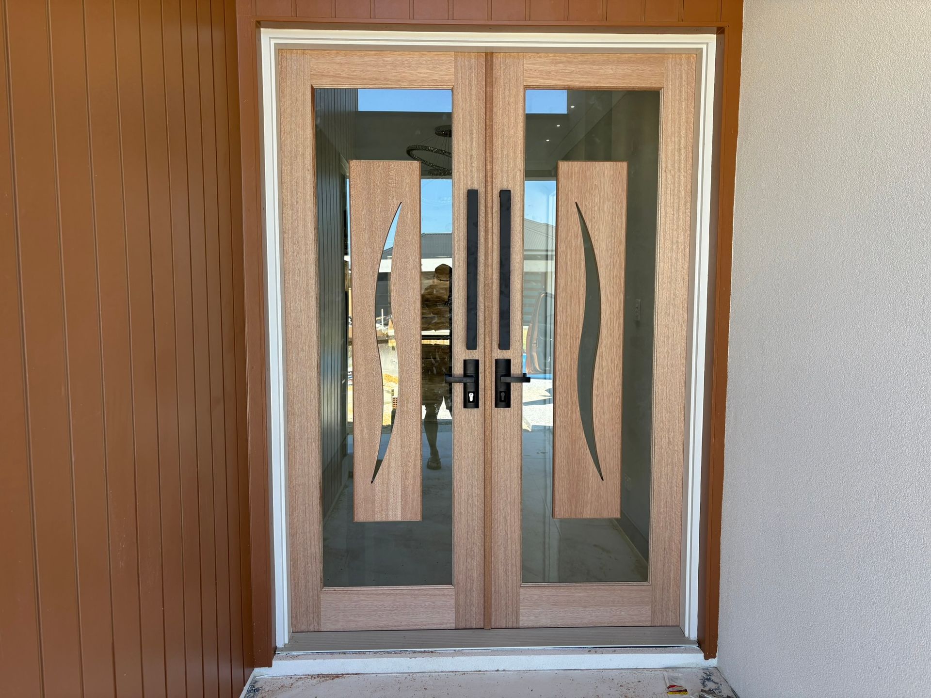 A person in work coveralls crouches while installing a white door frame seal into a threshold.