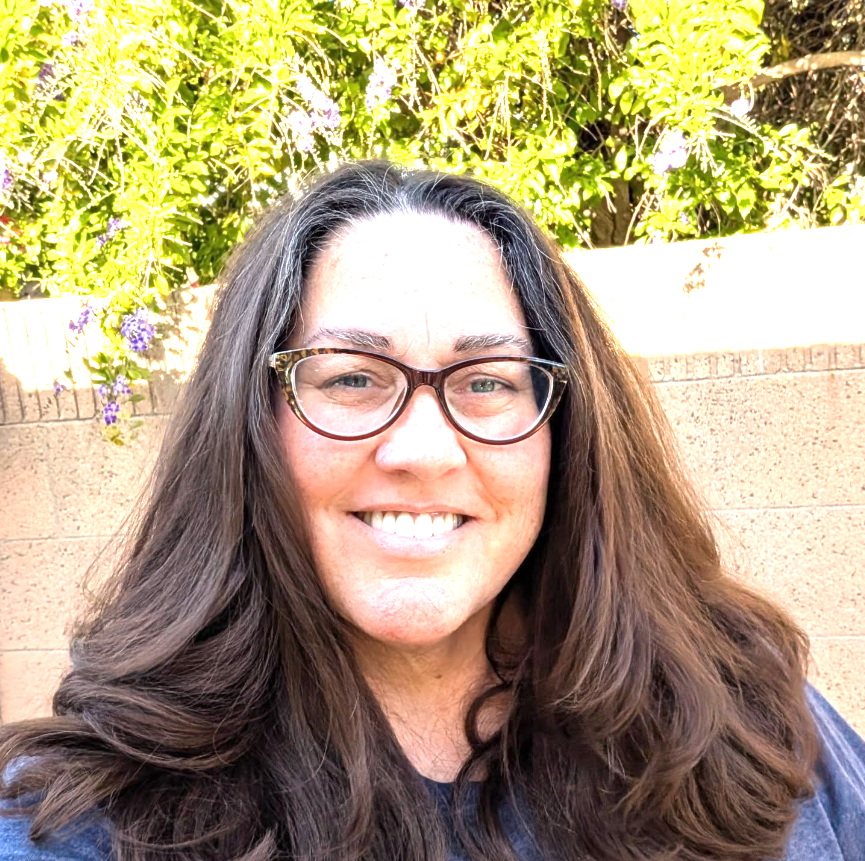 A woman with long hair and glasses is smiling for the camera.