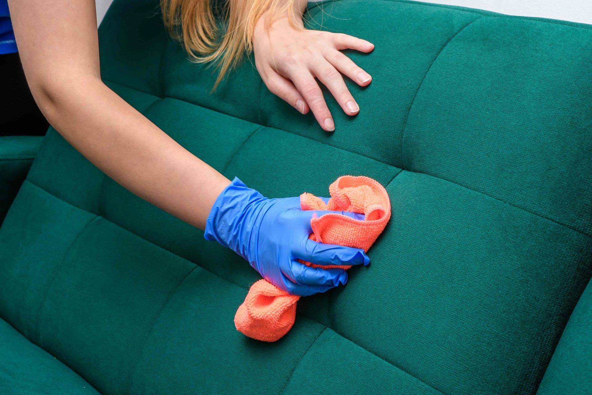 a woman is cleaning a green couch with a cloth and gloves