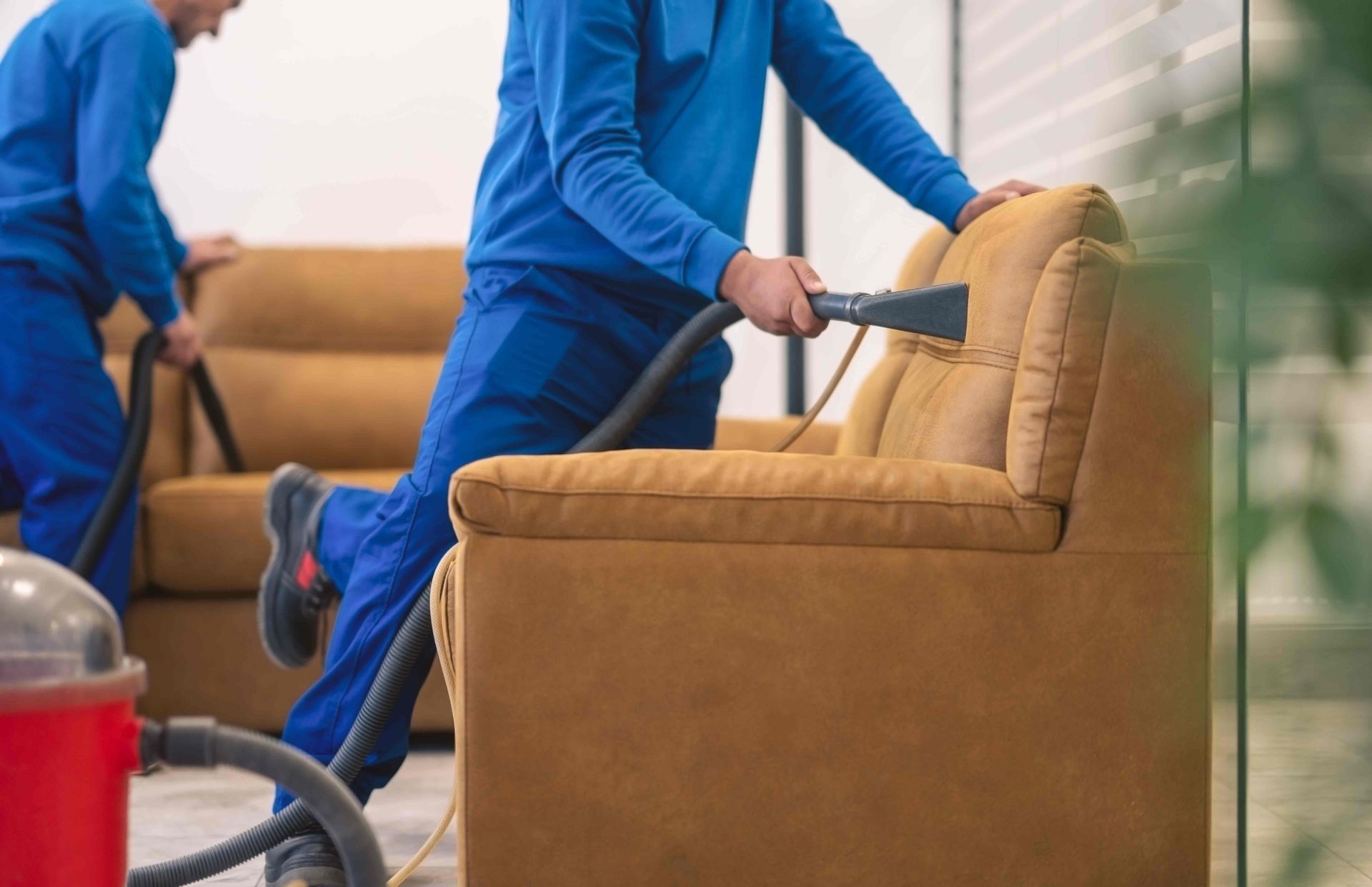 two men are cleaning a couch with a vacuum cleaner