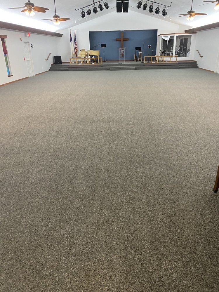 A large room with a carpeted floor and a cross on the wall.