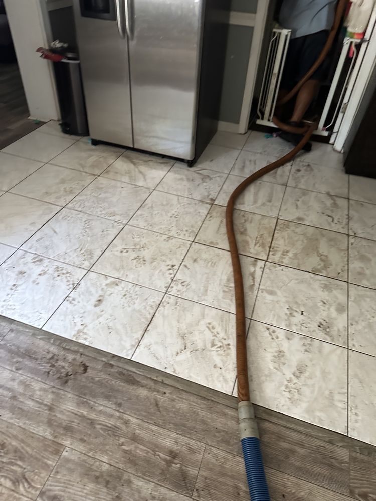 A hose is sitting on the floor in a kitchen next to a refrigerator.