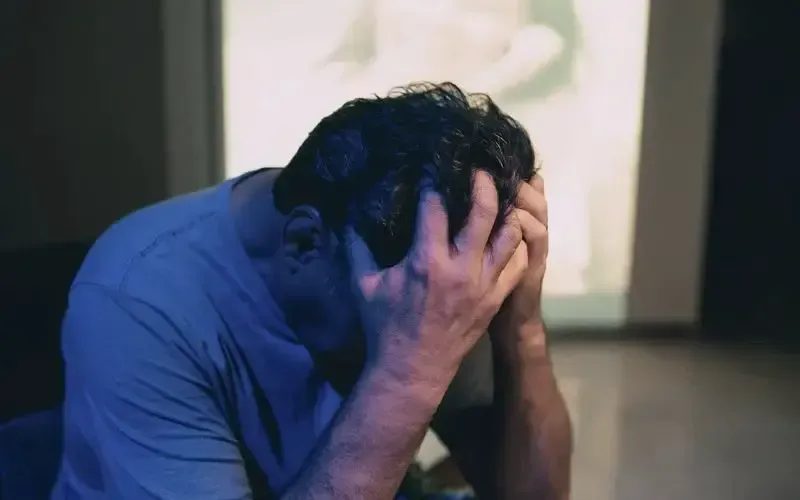 A man is covering his face with his hands in front of a projection screen.