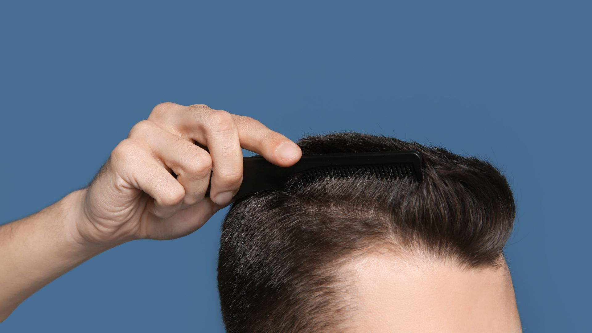 A man is combing his hair with a comb on a blue background.