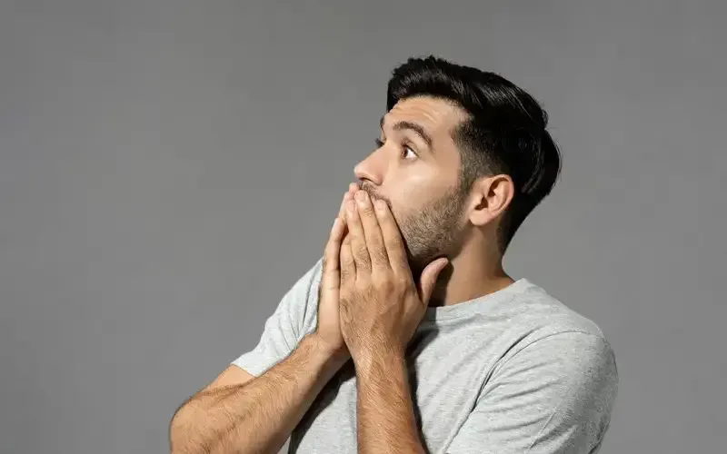 A man is covering his mouth with his hands and looking up.