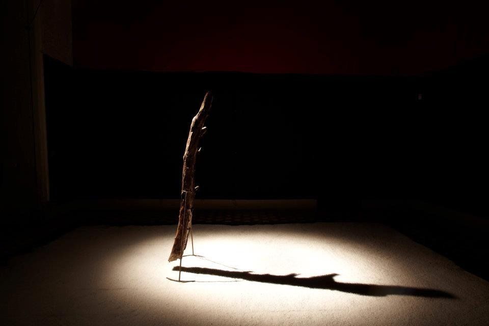 A sombra de um pedaço de pau é projetada no chão de uma sala escura.