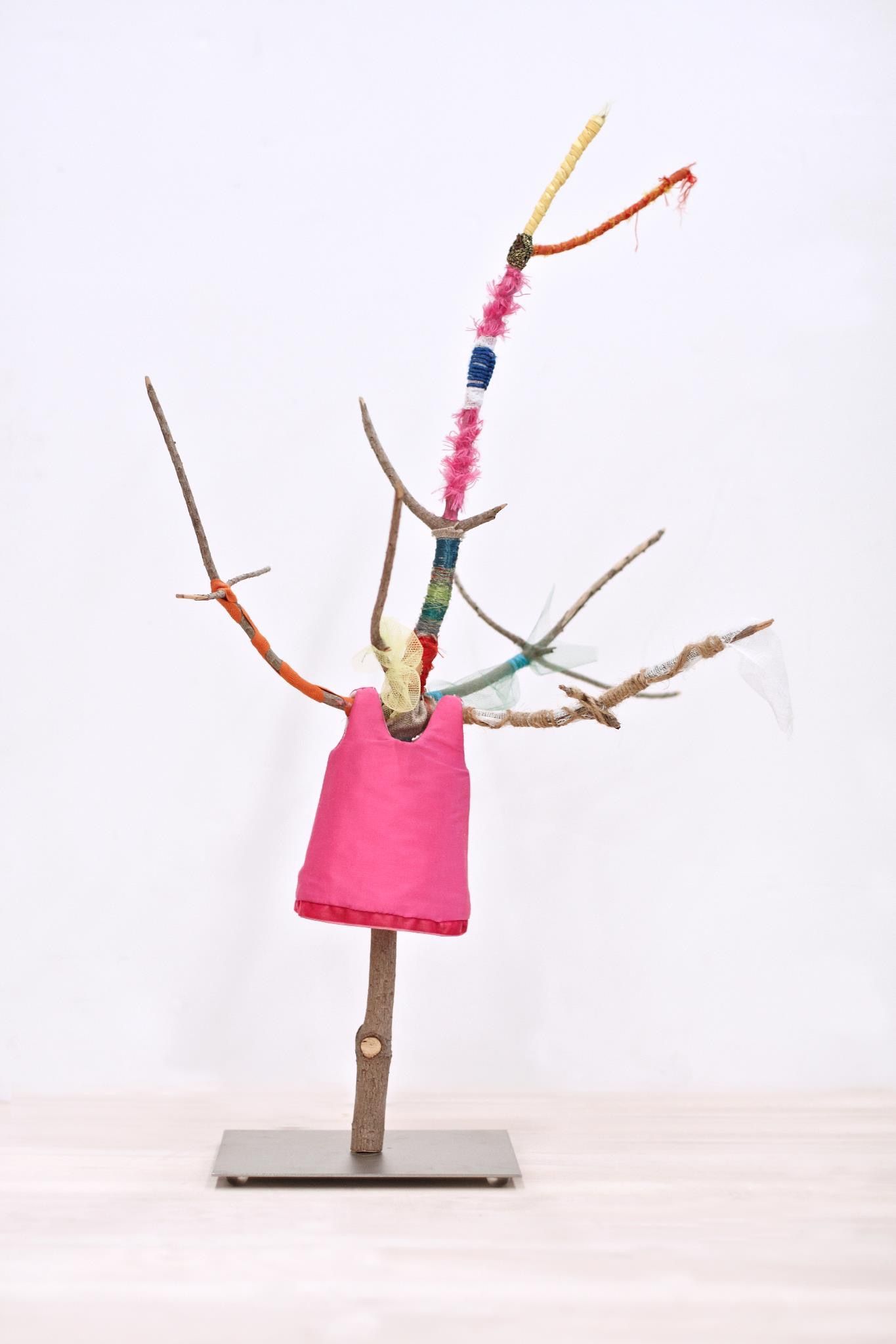 Uma escultura de uma árvore feita de galhos e um vaso rosa.