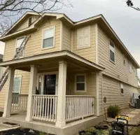 A two-story, yellow house with a white front porch and a ladder leaning against the left side.