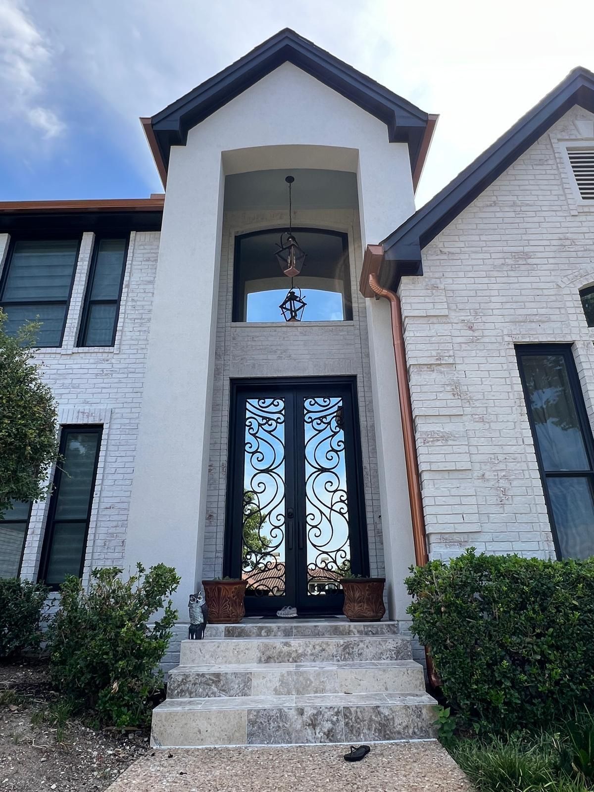 A two-story house with white stone siding, dark window frames, and an arched entryway with an ornate black metal door.