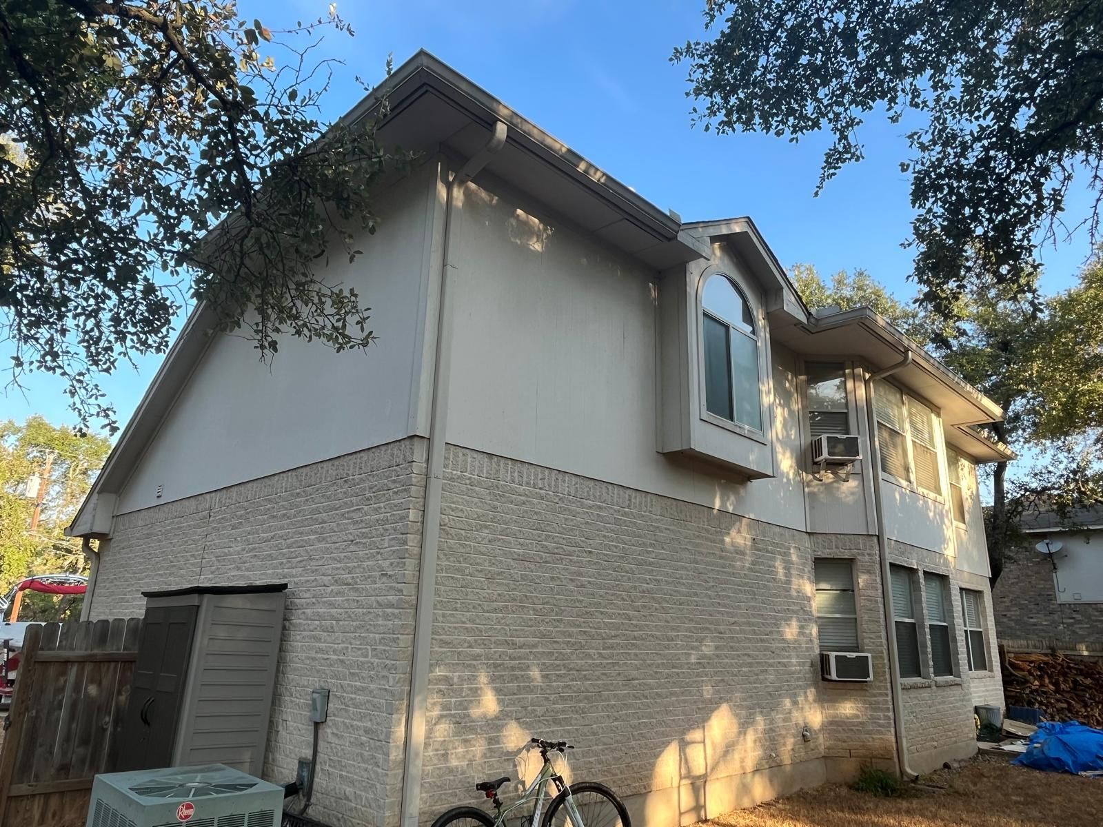 A two-story house exterior featuring beige painted siding on the upper level and textured off-white brick on the bottom.