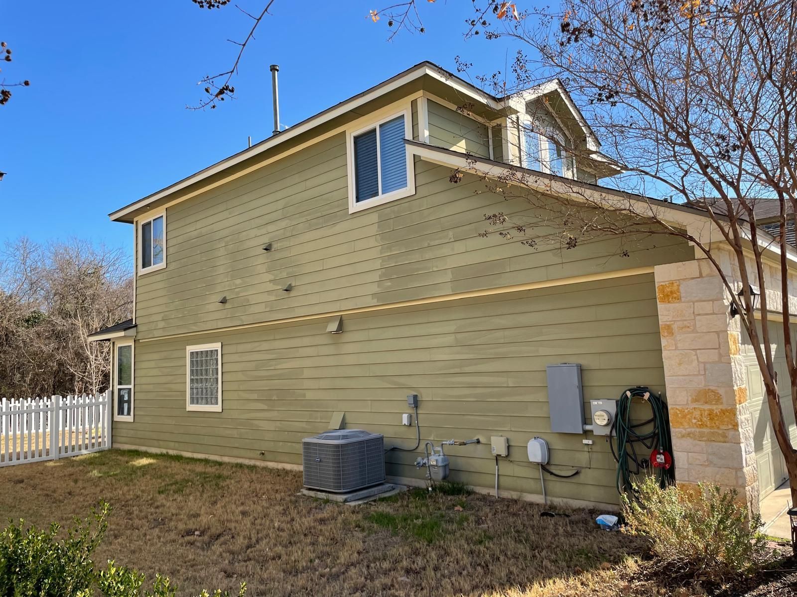 Side view of a two-story house with green horizontal siding, a stone accent wall, and an air conditioning unit on the lawn.