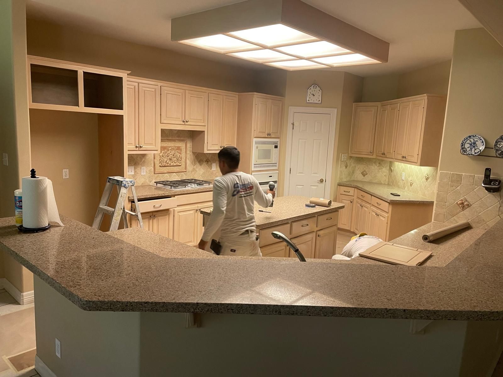 A person standing at a kitchen island in a room with light wood cabinets and a brown granite countertop.