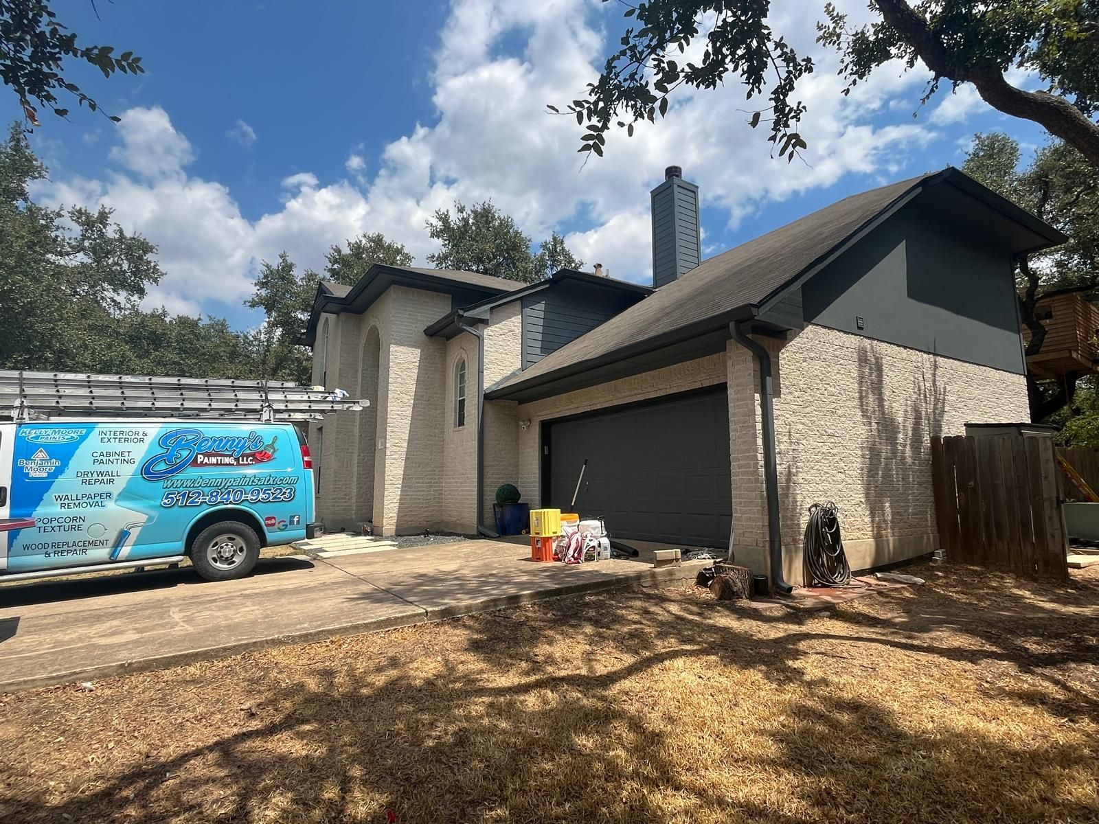 A light-colored stone home with dark trim and a garage, parked next to a blue service van under a blue sky.