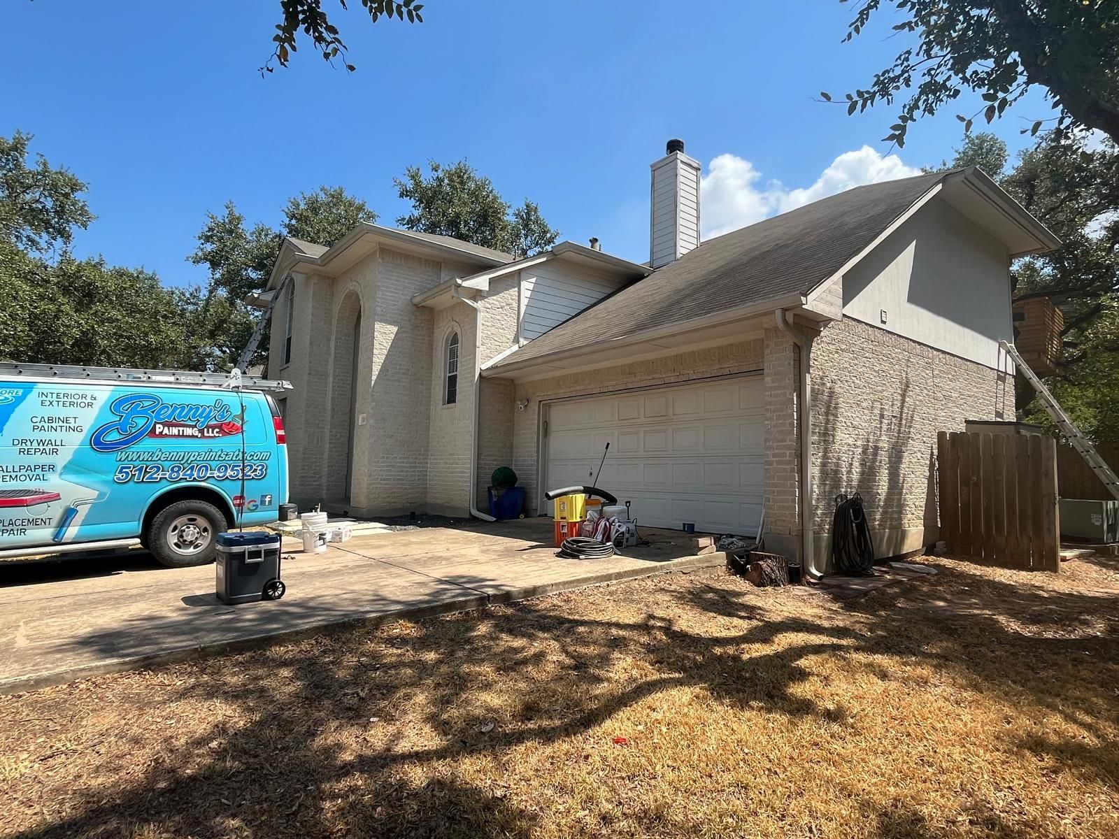 A blue service van is parked on the driveway of a light-colored brick house with a white garage door under a blue sky.