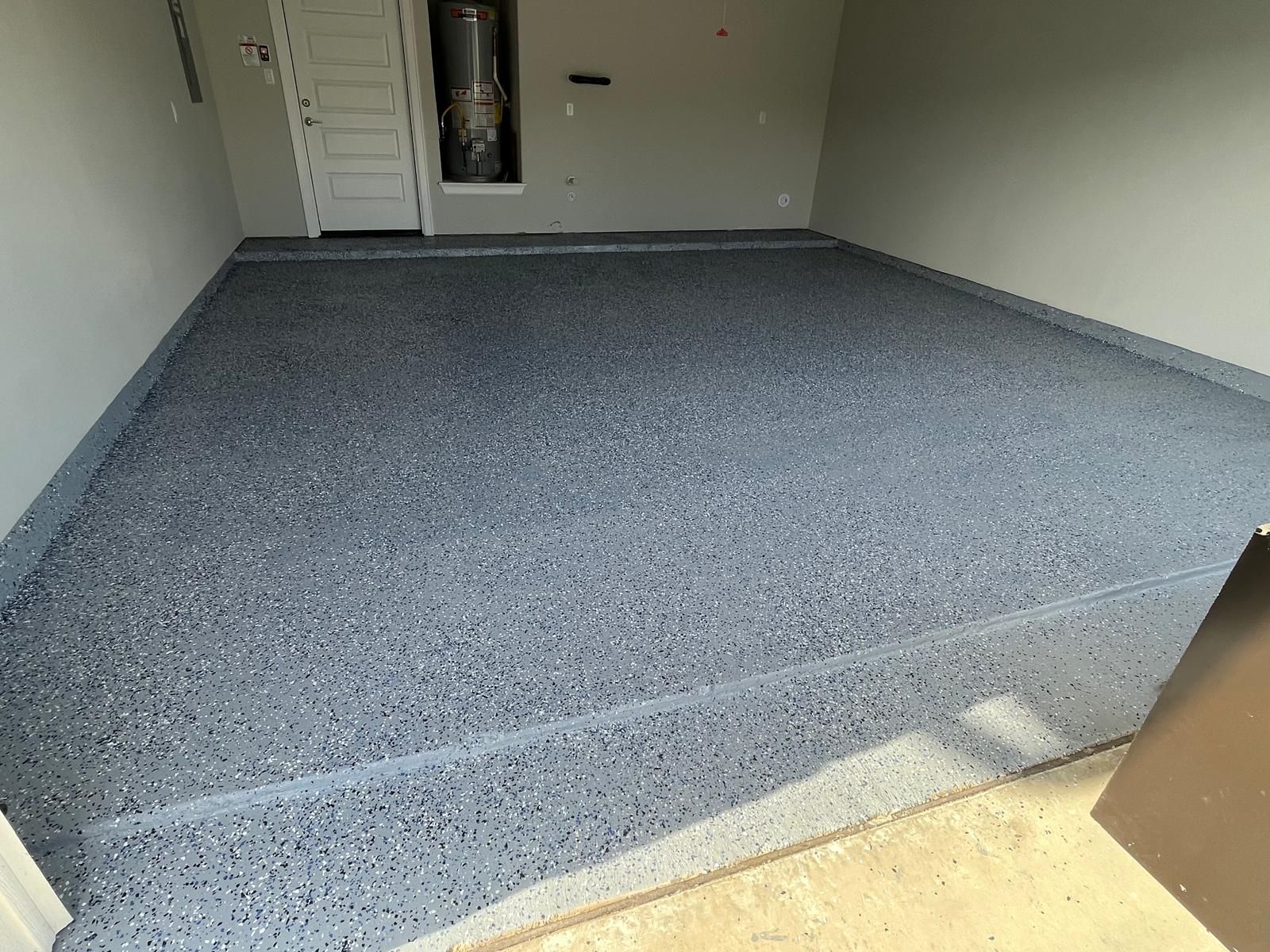 Garage floor with a gray, speckled epoxy finish, showing a clean, smooth surface leading to a doorway and water heater.