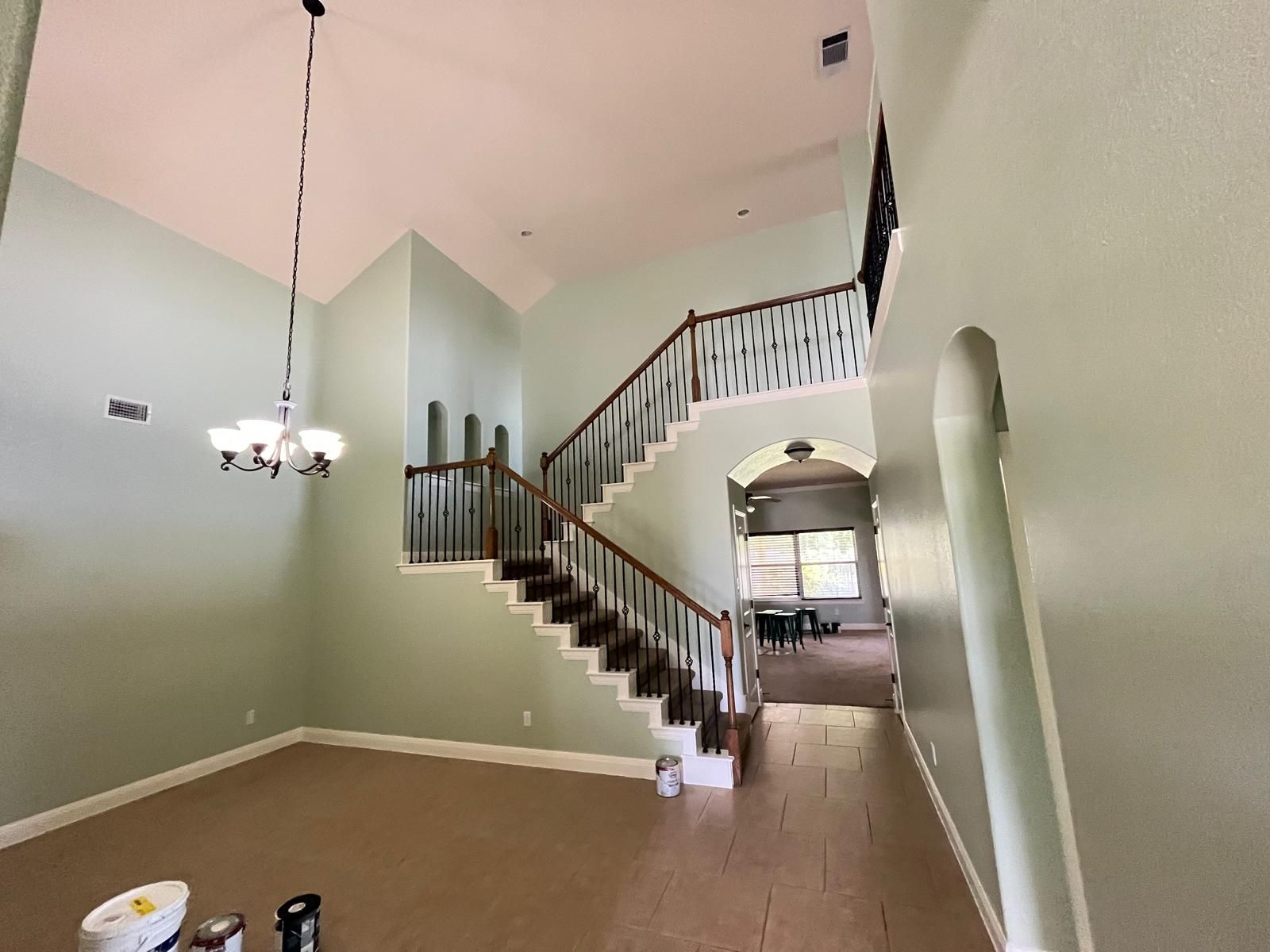 An open foyer with light green walls, a chandelier, and a carpeted staircase leading to a landing with a white railing.