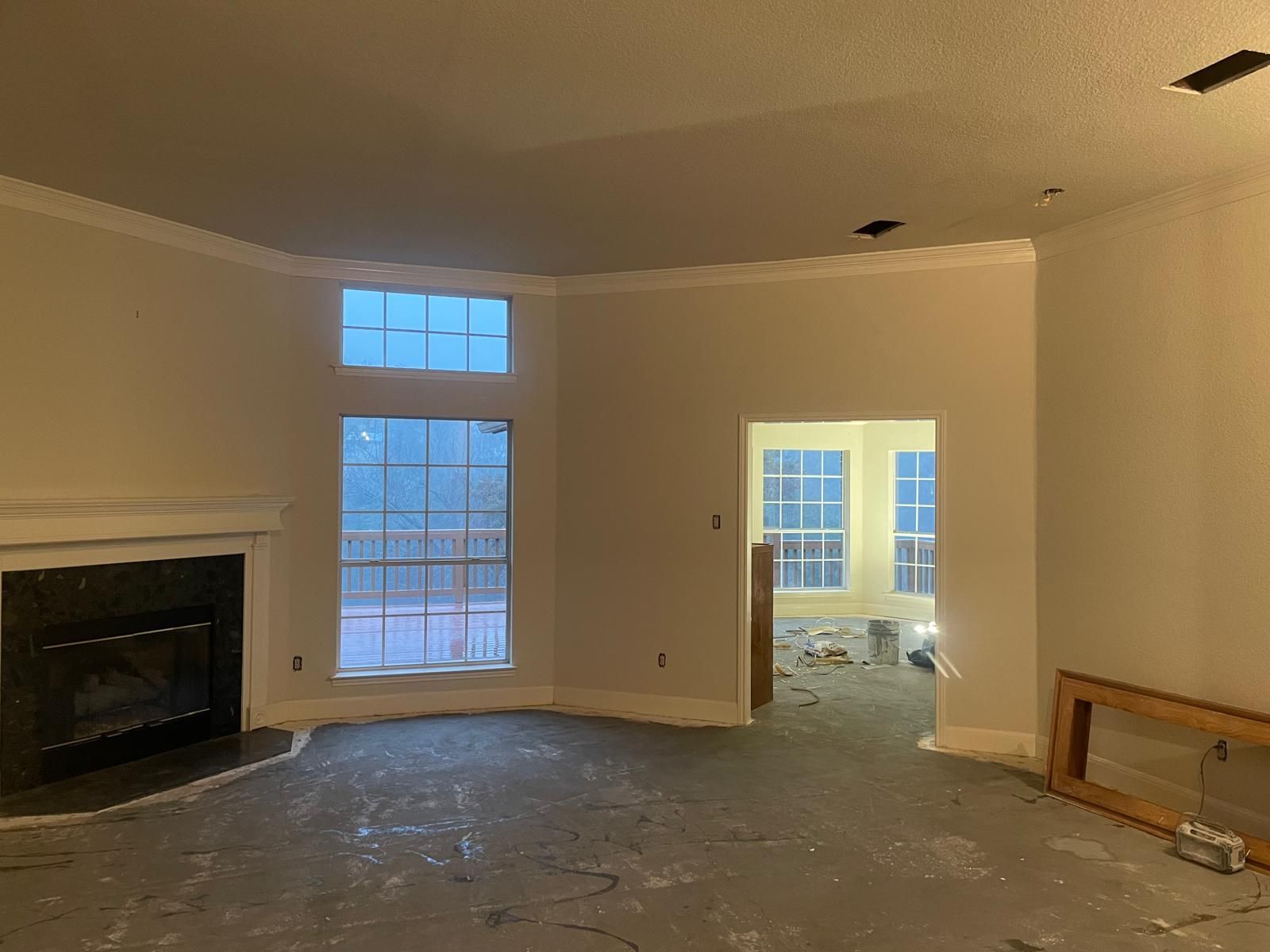An empty room under construction with light-colored walls, a stone fireplace, large windows, and a subfloor.