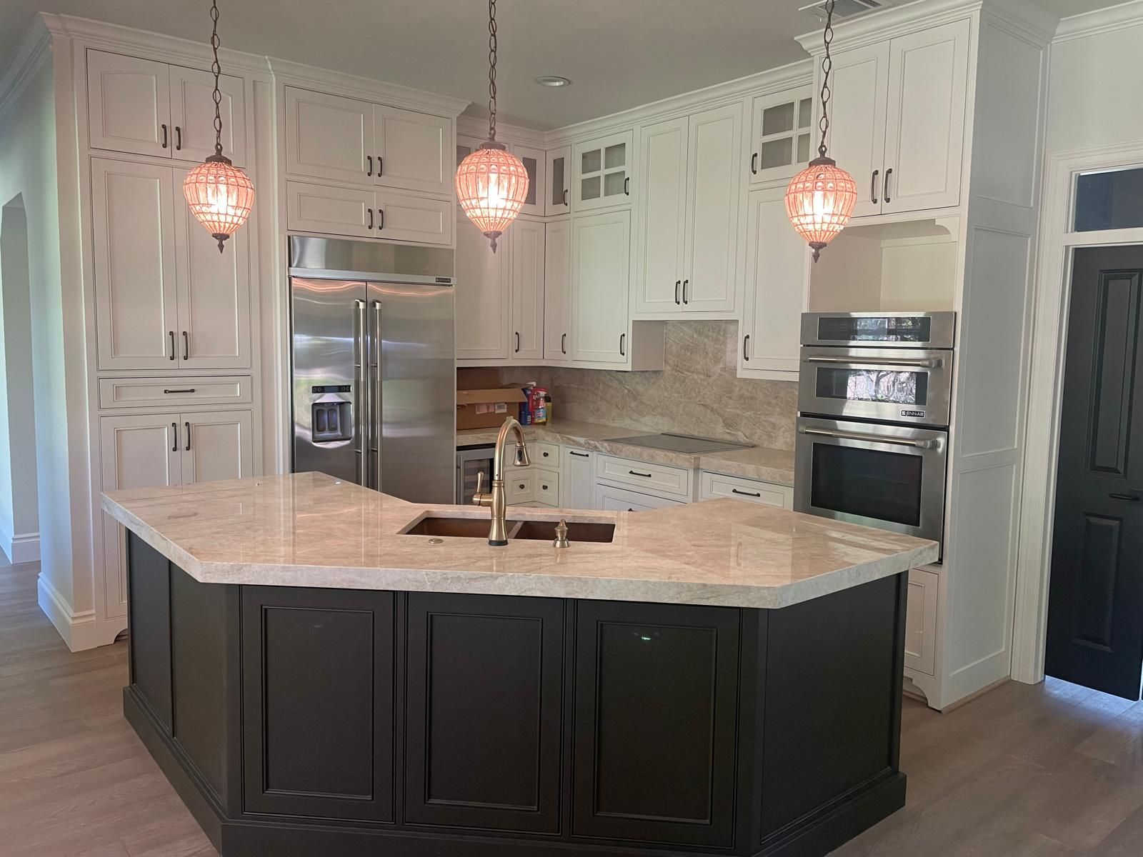A kitchen featuring white perimeter cabinets, a dark charcoal island with a light stone countertop, and three pendants.